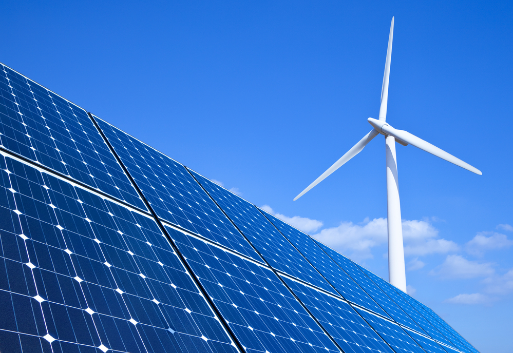 Solar panels and wind turbine against blue sky